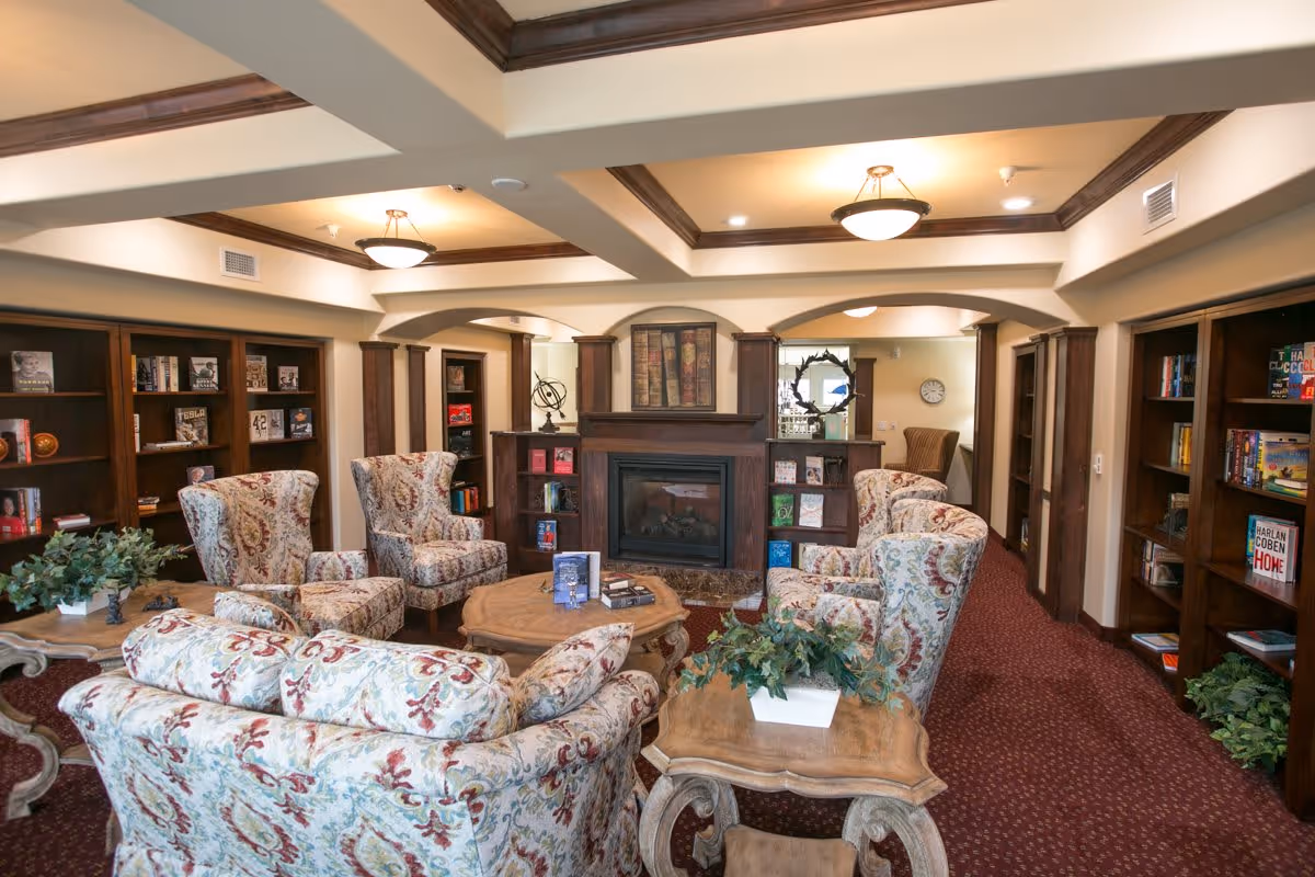 Cozy communal lounge with patterned armchairs arranged around a coffee table and fireplace, flanked by built-in bookshelves.