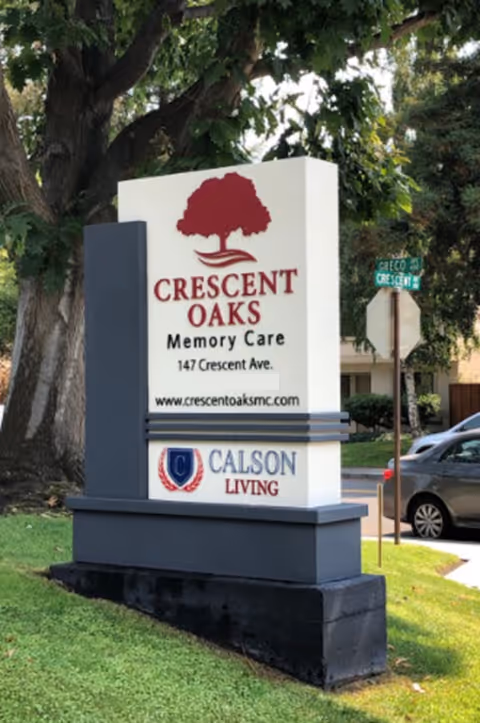 A large outdoor sign for Crescent Oaks Memory Care at a street corner.