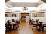 Dining room with several wooden tables and chairs, a chandelier, and a serving area with a clock on the back wall.