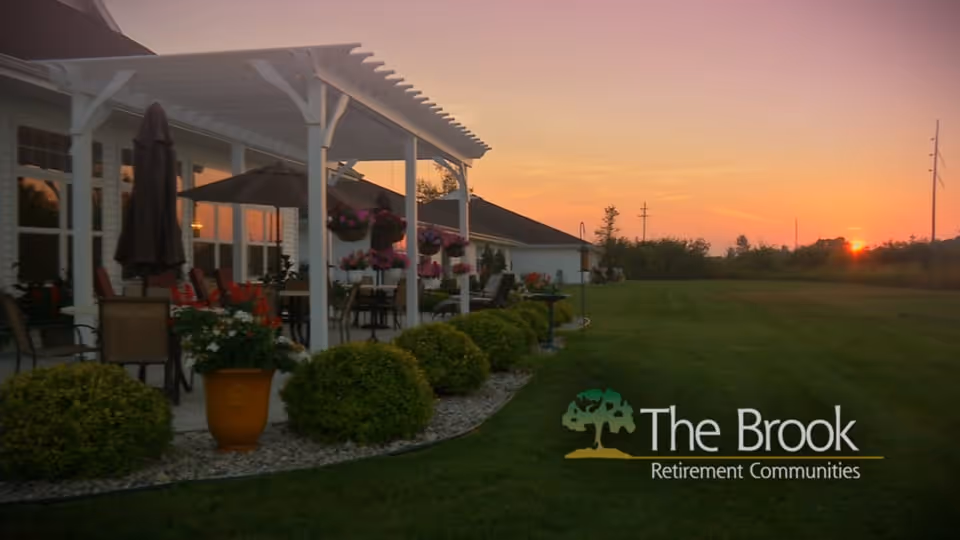 Sunset view of a pergola-covered patio with outdoor seating and landscaped lawn beside a retirement community building.