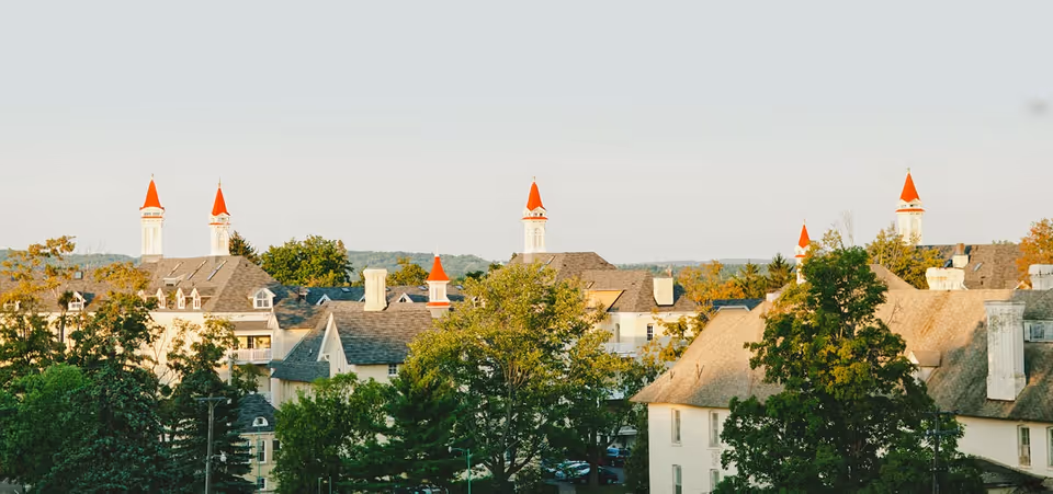 View of a senior living facility with multiple buildings featuring steep roofs and red pointed towers, surrounded by trees and greenery under a clear sky.