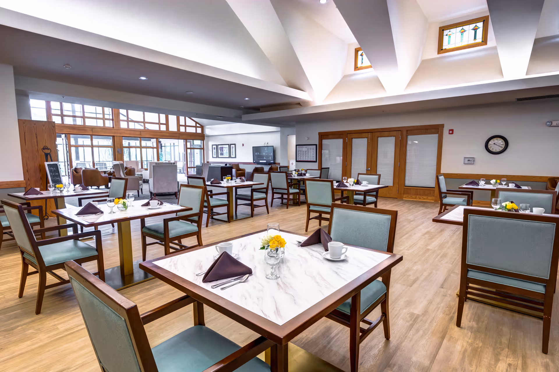 Spacious, well-lit dining room with multiple set tables and chairs, skylights, and wooden accents.