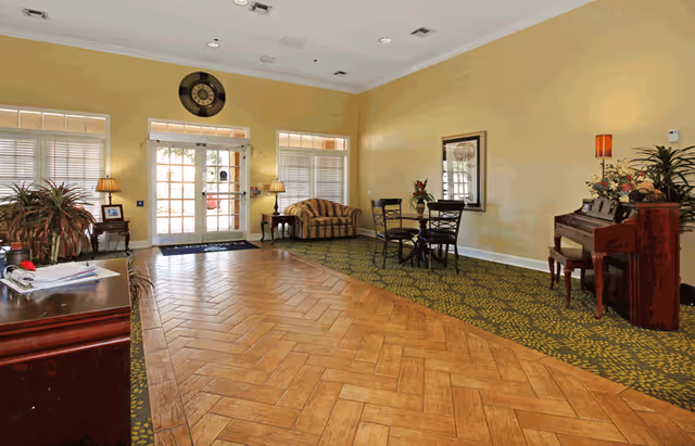 Spacious senior living facility lobby with seating, a piano, and glass double doors letting in natural light.