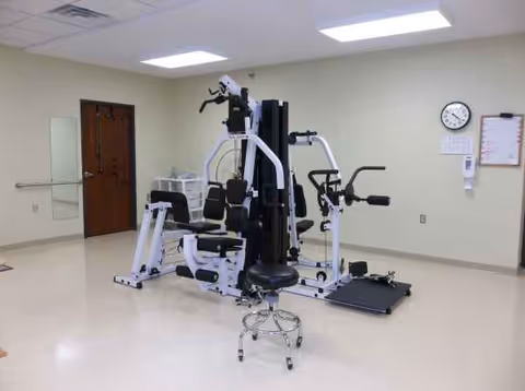 Pine Crest Nursing Home rehab gym with weight machines and a rolling chair.