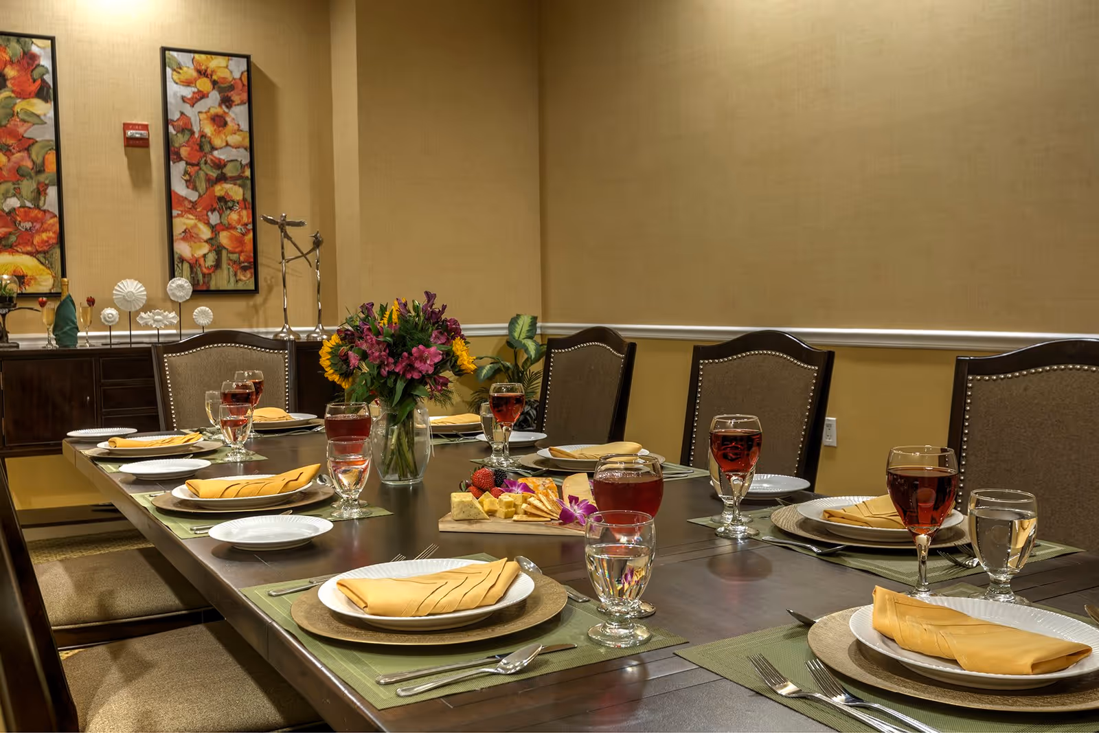 Formally set dining table in a dining room with place settings, glasses of red beverage, a floral centerpiece, and chairs.