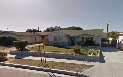 Single-story senior living facility with landscaped front yard and stone wall.