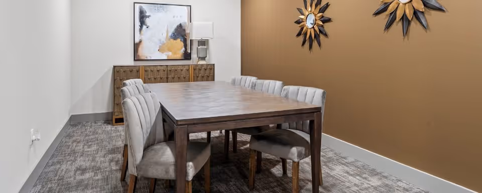 Small dining/meeting room with a wooden table surrounded by upholstered chairs, a sideboard, and wall art.