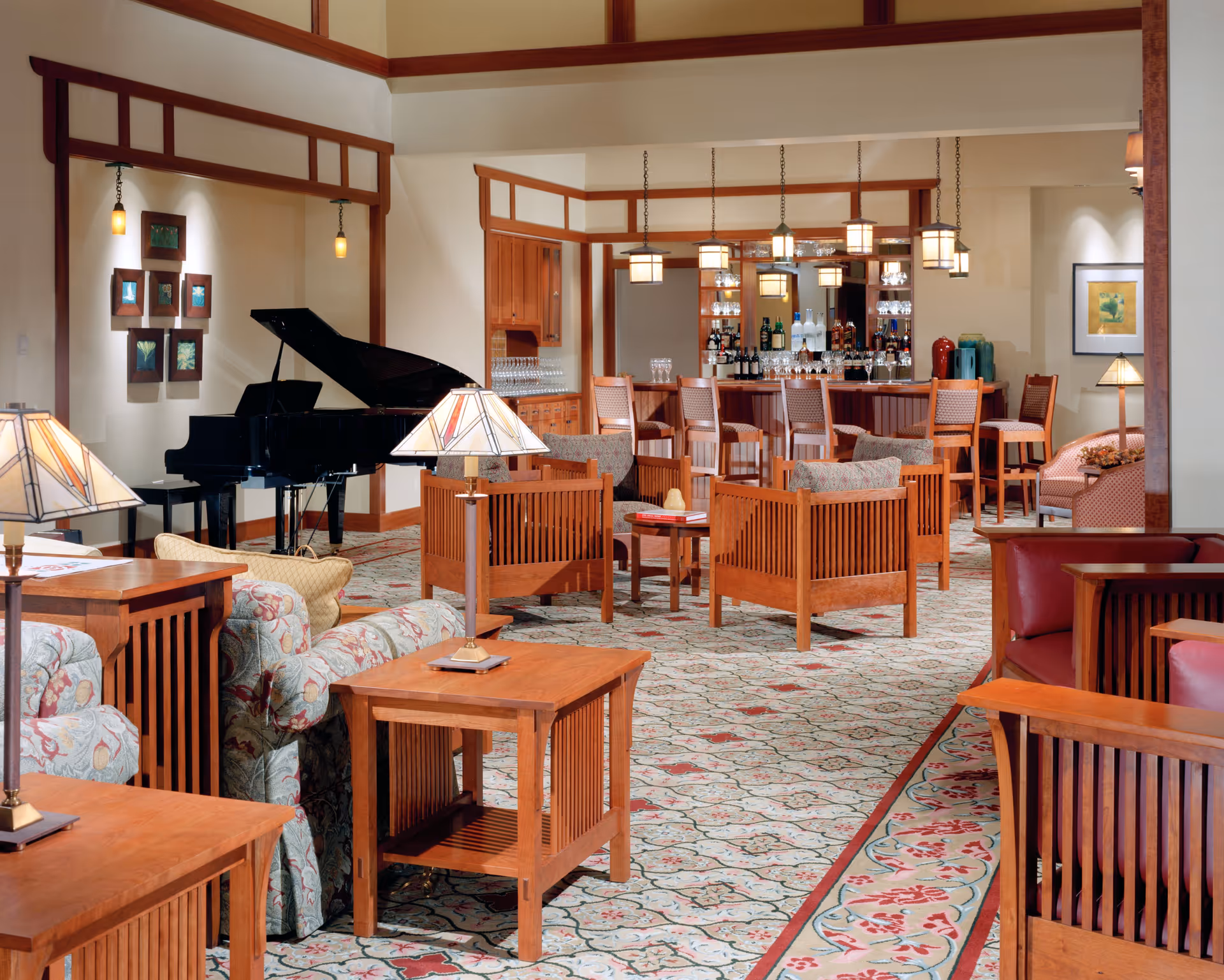 Spacious senior living lounge with wooden chairs and tables, patterned carpet, a grand piano and a bar in the background.