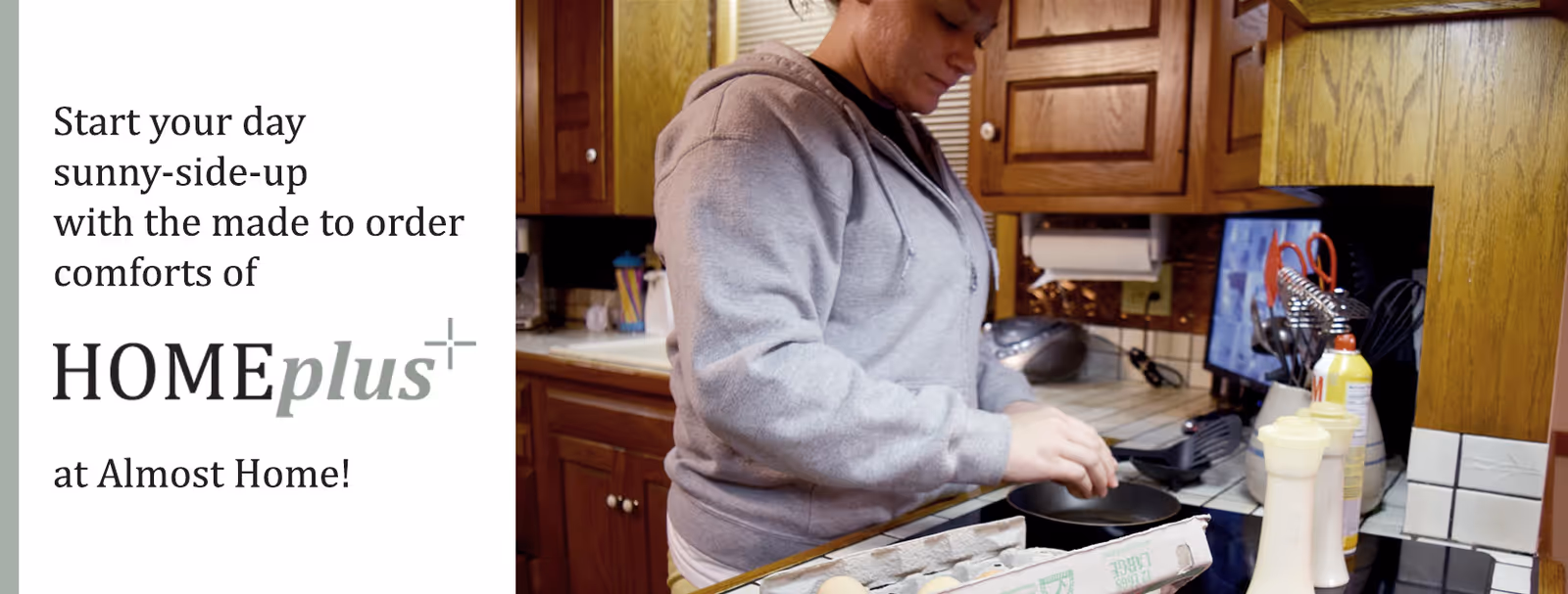 A person in a gray hoodie cooking in a kitchen with wooden cabinets, preparing to fry eggs in a pan. There are various kitchen items on the counter including an egg carton, cooking spray, and utensils. Text on the left side reads: 'Start your day sunny-side-up with the made to order comforts of HOMEplus at Almost Home!'