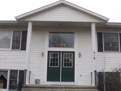 Front entrance of a white senior living home with green doors and pillars