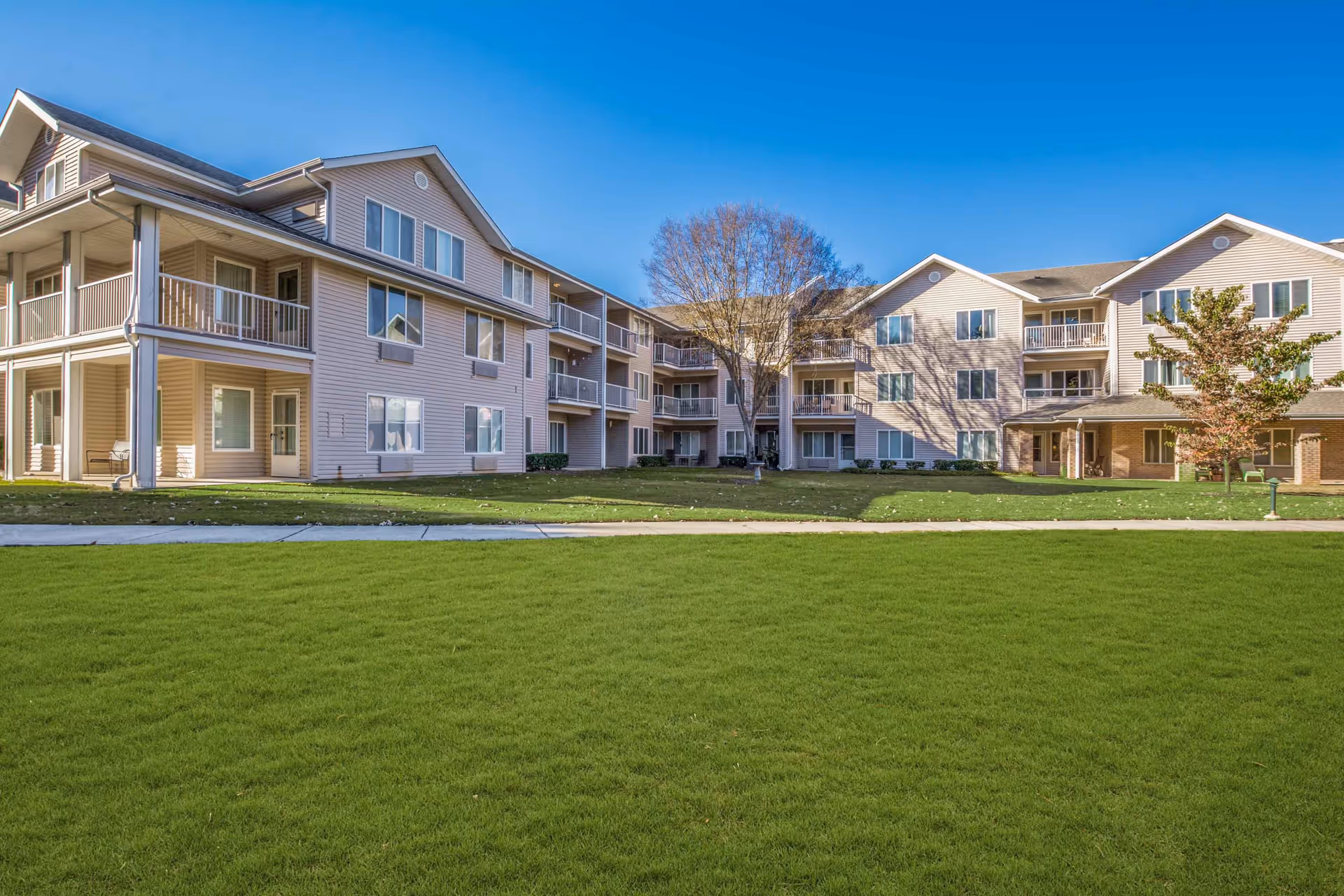 Front exterior of a three-story residential building with balconies overlooking a large green lawn.