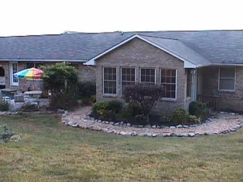 A single-story brick senior care facility facade with manicured landscaping and curved stone border.