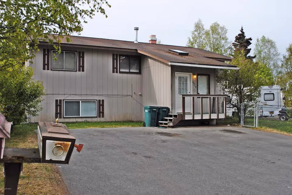 Front exterior of a two-story beige house with a small porch, driveway, mailbox, and trash bins.