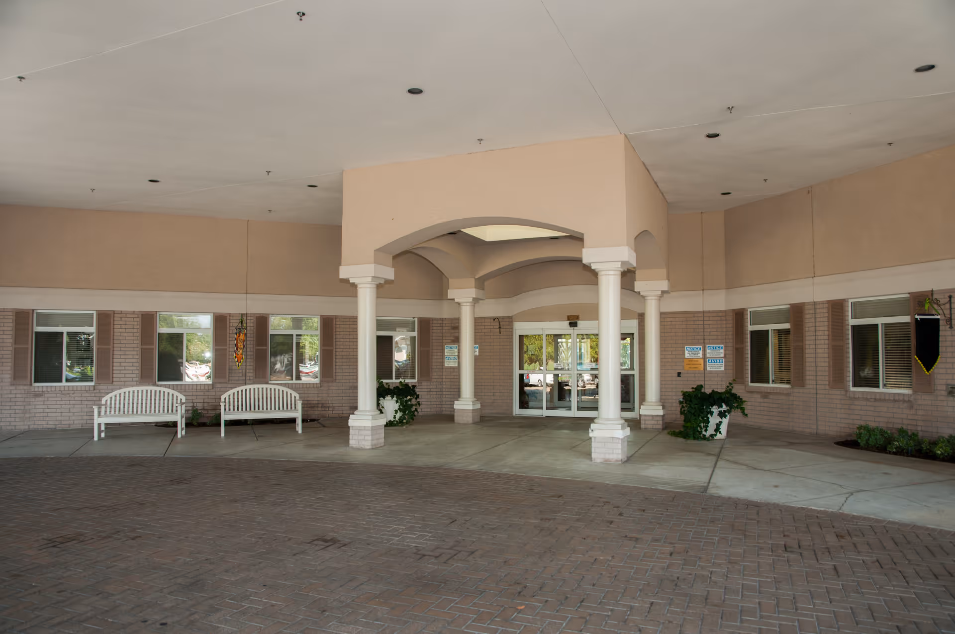 Covered porte-cochère entrance with columns, white benches, potted plants, and glass double doors.