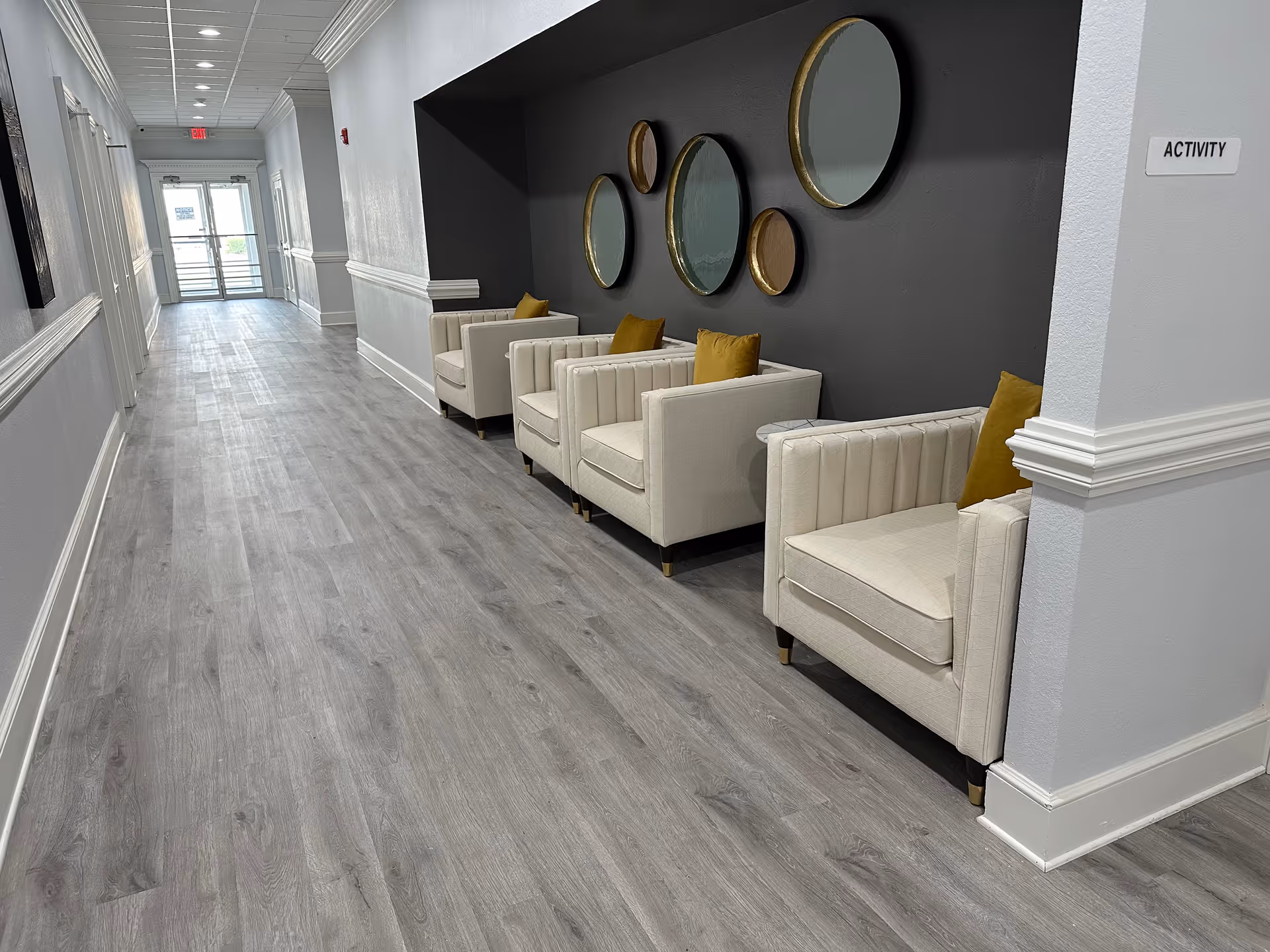 A bright hallway seating area with four beige armchairs and circular mirrors on a dark accent wall.