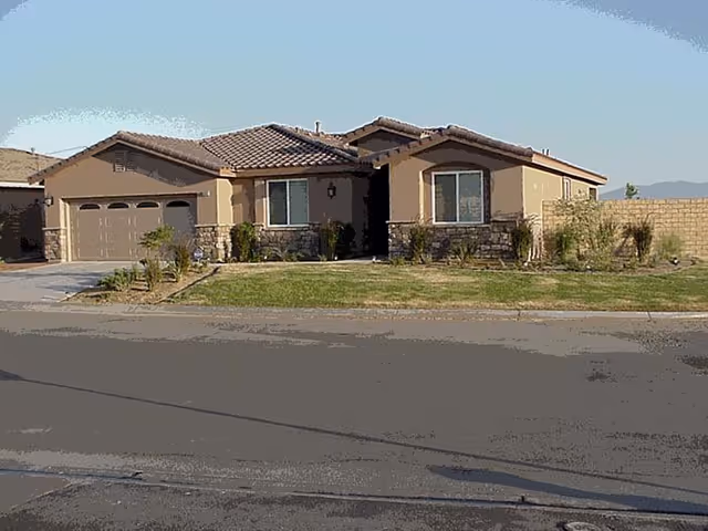 Single-story beige stucco house with a tiled roof, attached garage, stone accents, and a front lawn.