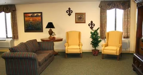 A seating area with a striped sofa, two yellow armchairs, a side table with lamp, wall art, and curtained windows.