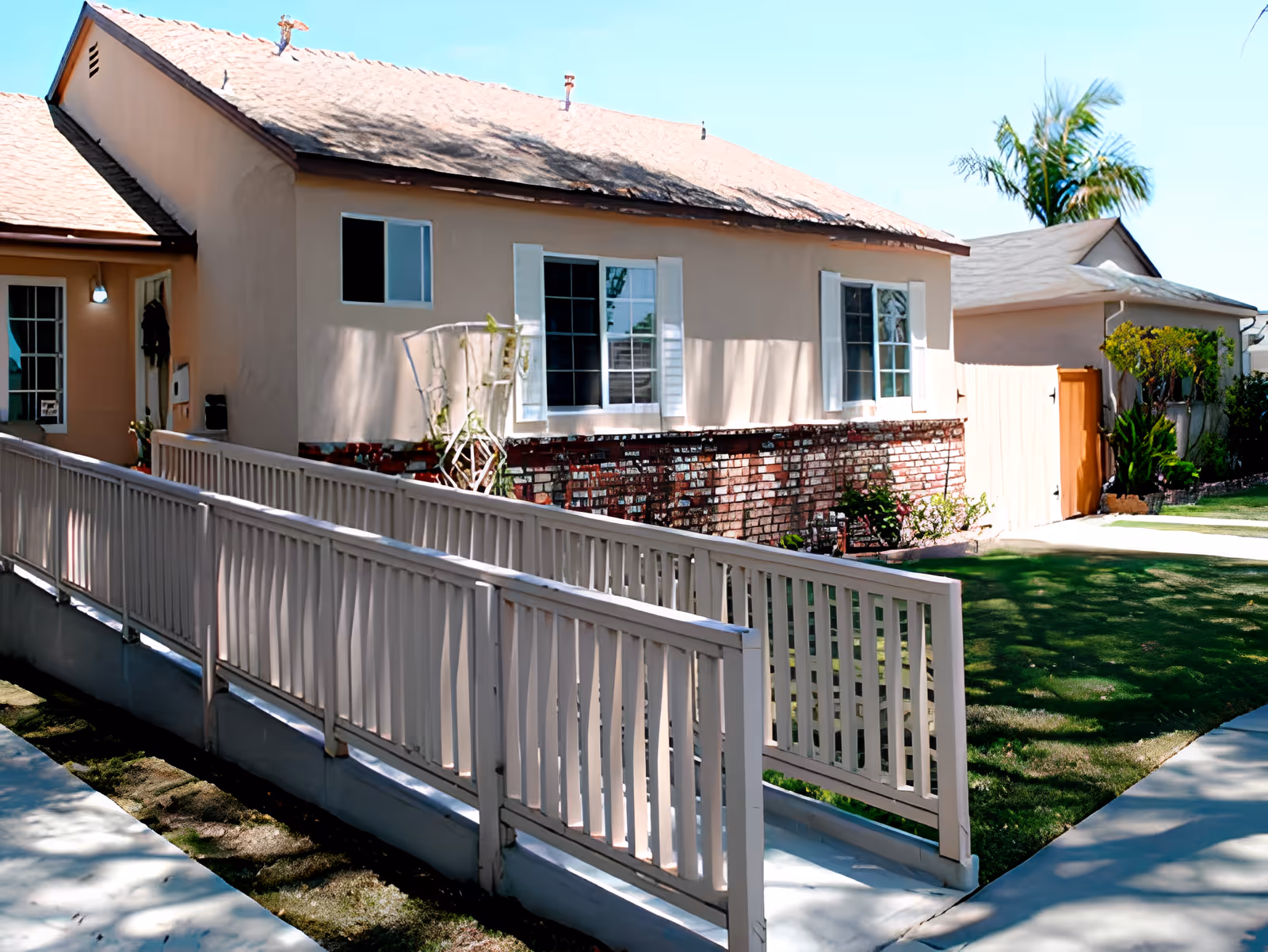 Single-story beige house with a wheelchair ramp leading to the front entrance, brick foundation, and a small lawn.