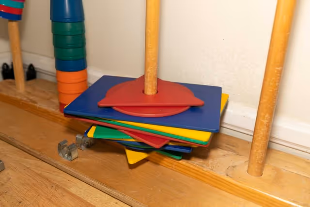 Close-up of a children's stacking toy with colorful plastic shapes on a wooden peg and base.