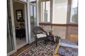 Enclosed sunroom with a wicker chair, small side table with plants, a patterned area rug, and glass French doors leading inside.
