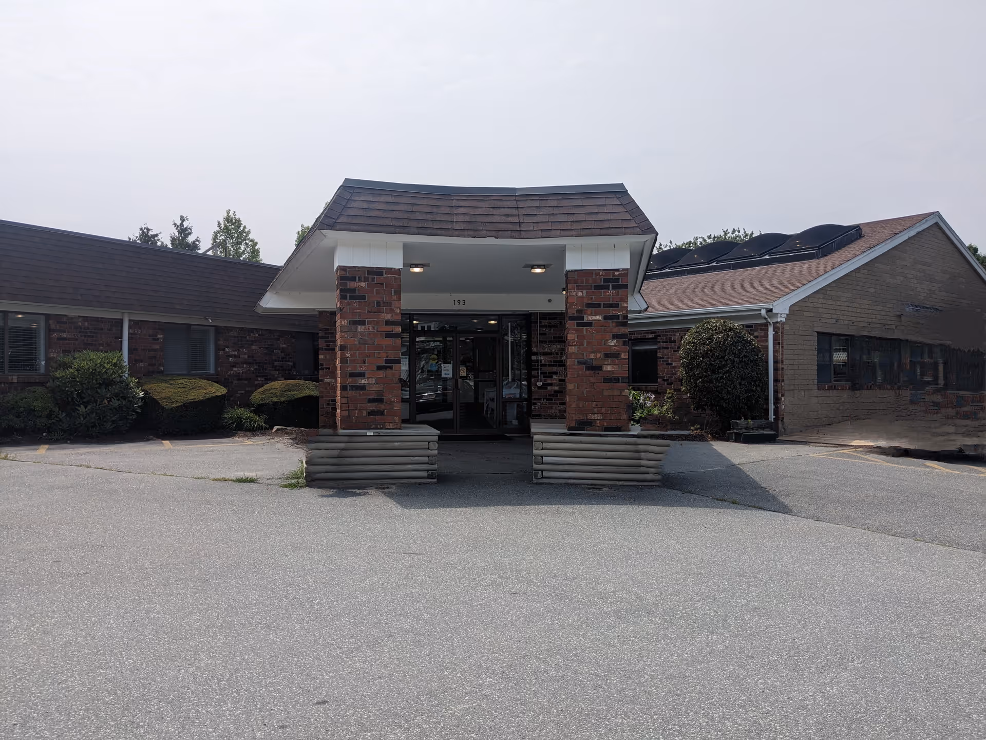 Front entrance of a single-story brick nursing facility with a covered drive-up portico and parking area.