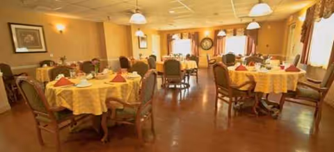 Interior dining room with round tables, yellow tablecloths, and residents seated.