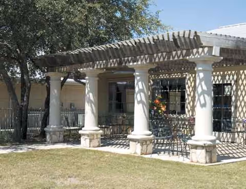 Outdoor patio with a wooden pergola, columns, and seating beside a building.