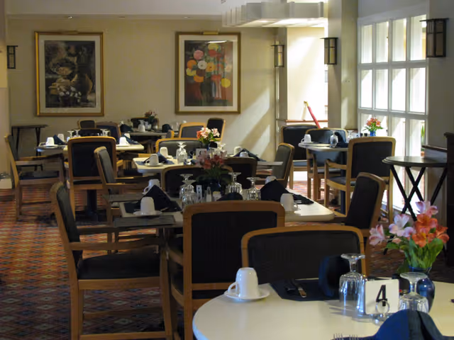 Dining room with multiple tables and chairs set with dishes, glassware, napkins, and floral centerpieces.