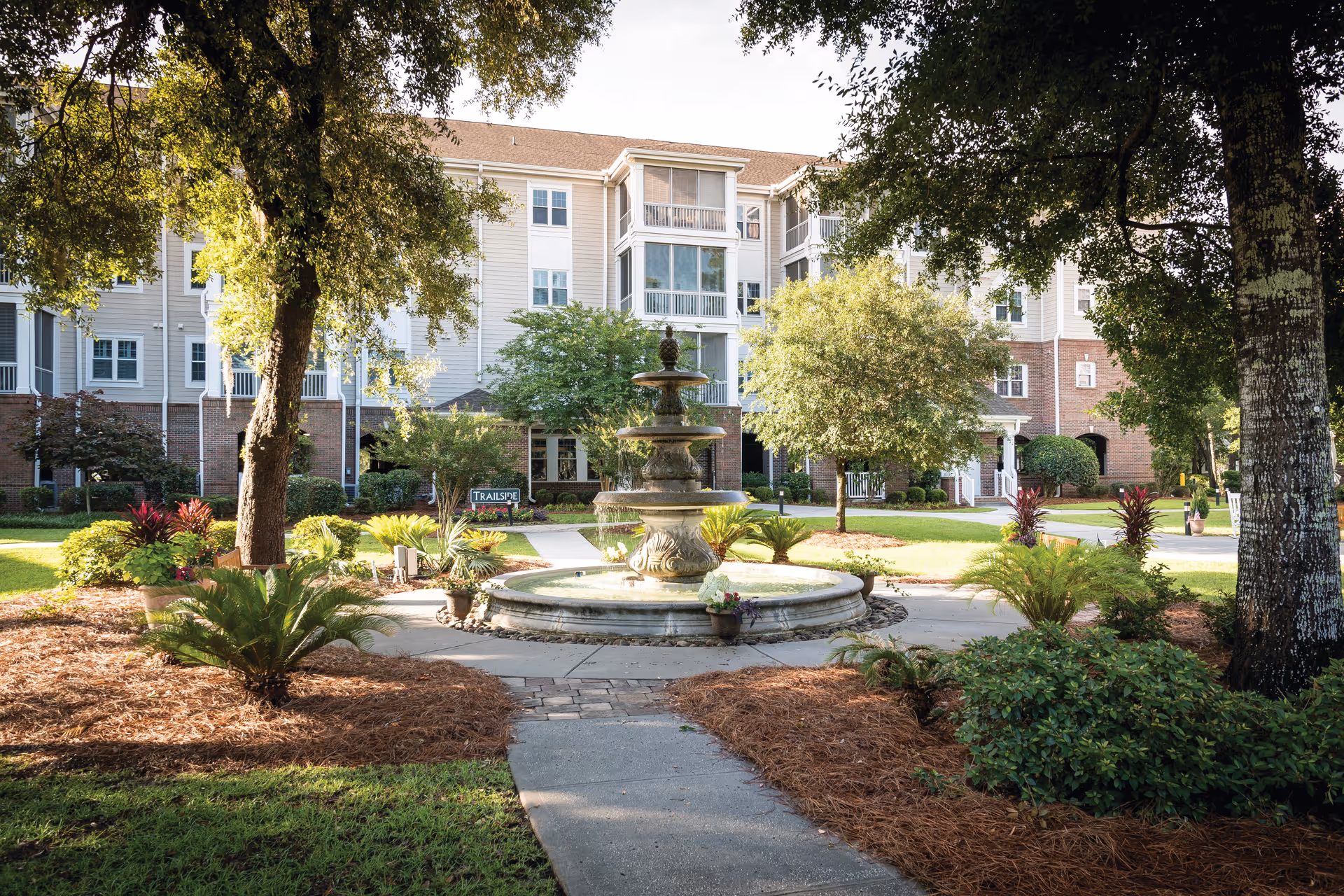 Courtyard with a tiered fountain and landscaped gardens in front of a multi-story senior living building.