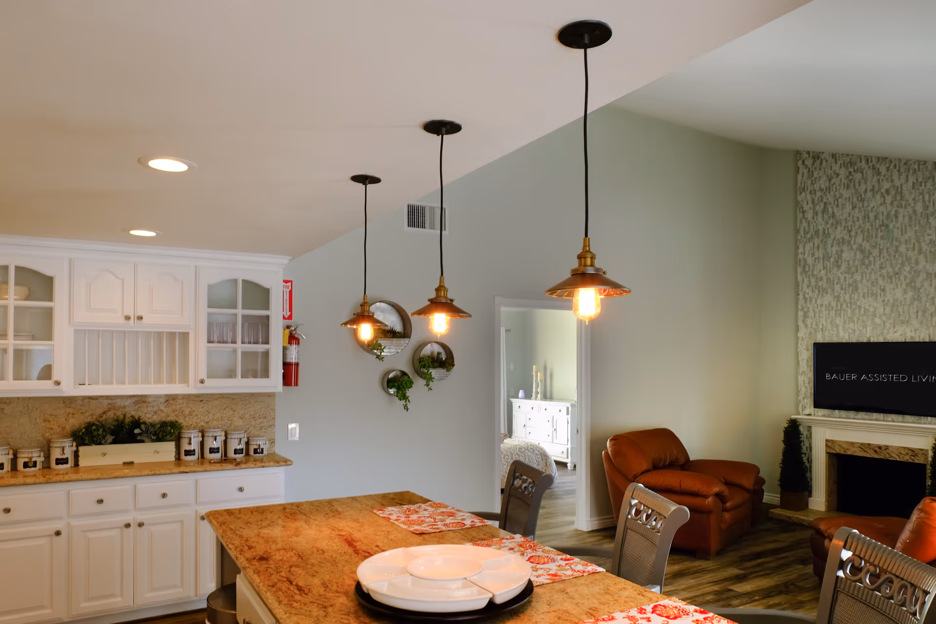 Open-plan kitchen with a marble island and pendant lights overlooking a living area with leather chairs and a TV.