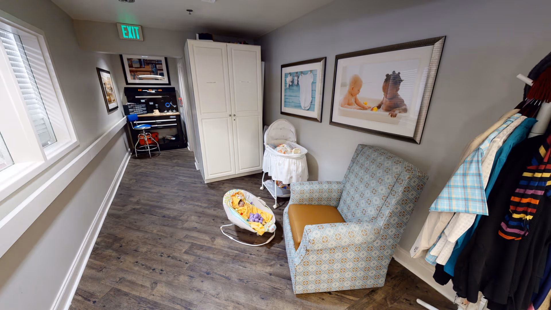 Hallway seating area with an upholstered armchair, baby bassinet and rocker, cabinets and a coat rack.