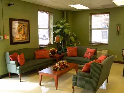 Green-walled living room in a senior facility with couches, red cushions, and a coffee table.