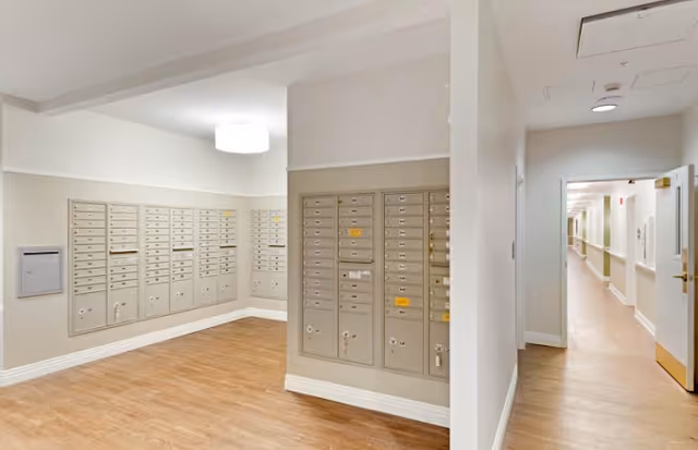 Interior mailroom area with rows of wall-mounted mailboxes and a hallway leading further into the facility.
