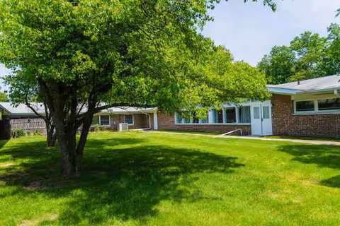 Brick senior care center exterior with green lawn, trees, and a walkway.