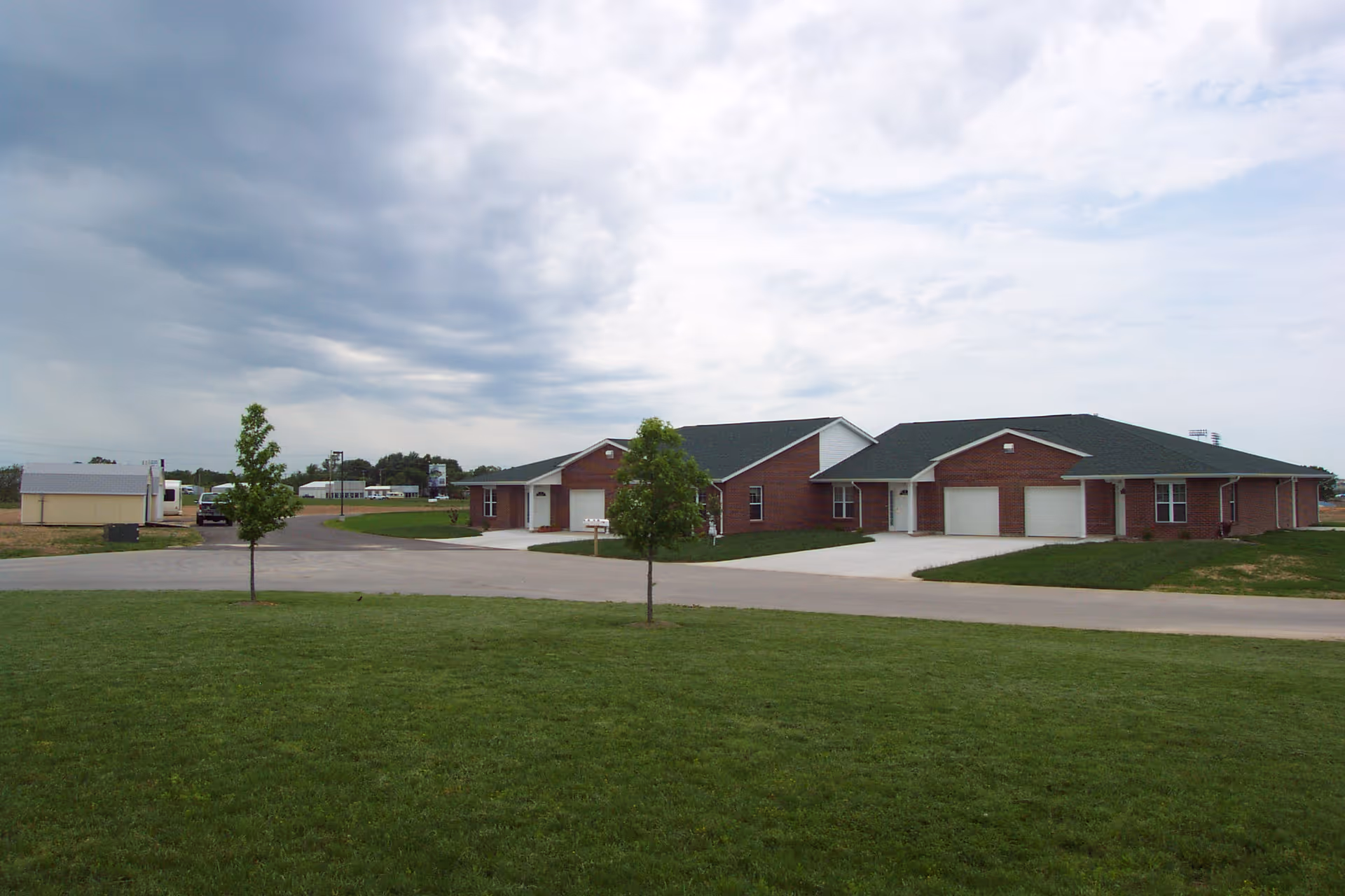 Exterior view of a single-story brick building with green roofs, surrounded by a well-maintained lawn and a few small trees under a cloudy sky.