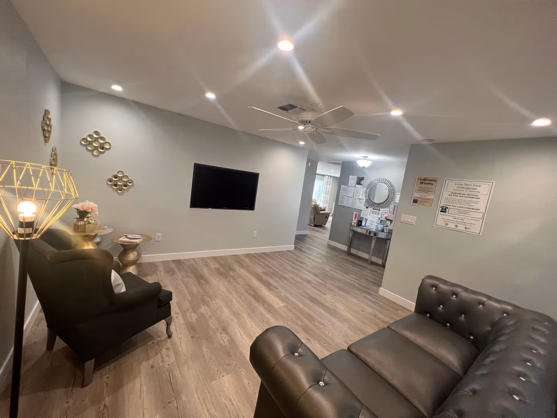 Spacious senior living common area with seating, a wall-mounted TV, decorative accents, and wood-look flooring.