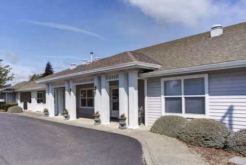 Single-story senior living building with entrance, columns, and landscaped shrubs along walkway.