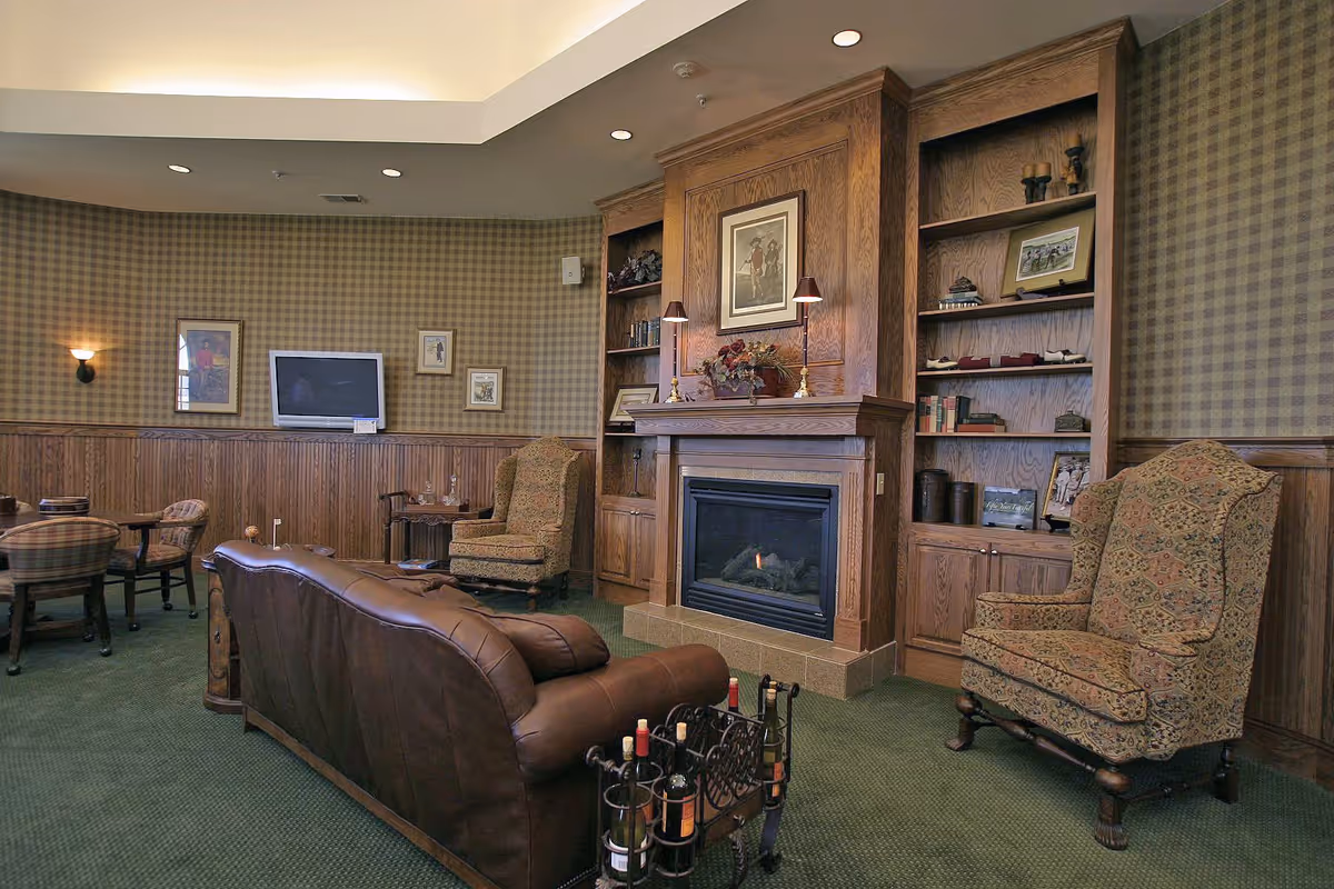 Cozy lounge with a leather sofa, patterned armchairs, a fireplace framed by built-in wooden bookshelves, and a wall-mounted TV.