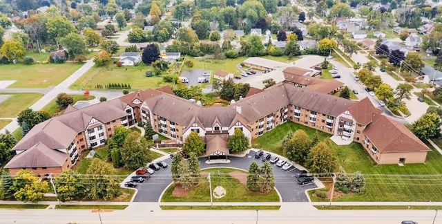 Aerial view of a large senior living facility named LakeHouse Sheboygan, showing a multi-wing building with brown roofs surrounded by green lawns, trees, parking areas, and a residential neighborhood in the background.