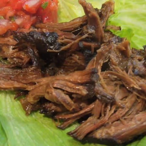 Close-up of shredded cooked meat served on a bed of lettuce with a side of diced tomatoes.