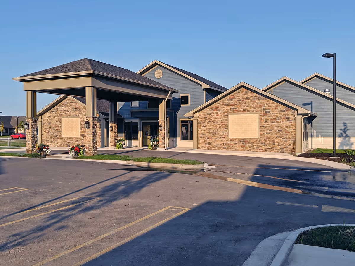 Front entrance of a brick-and-siding retirement community with a covered porte-cochère and adjacent parking lot.