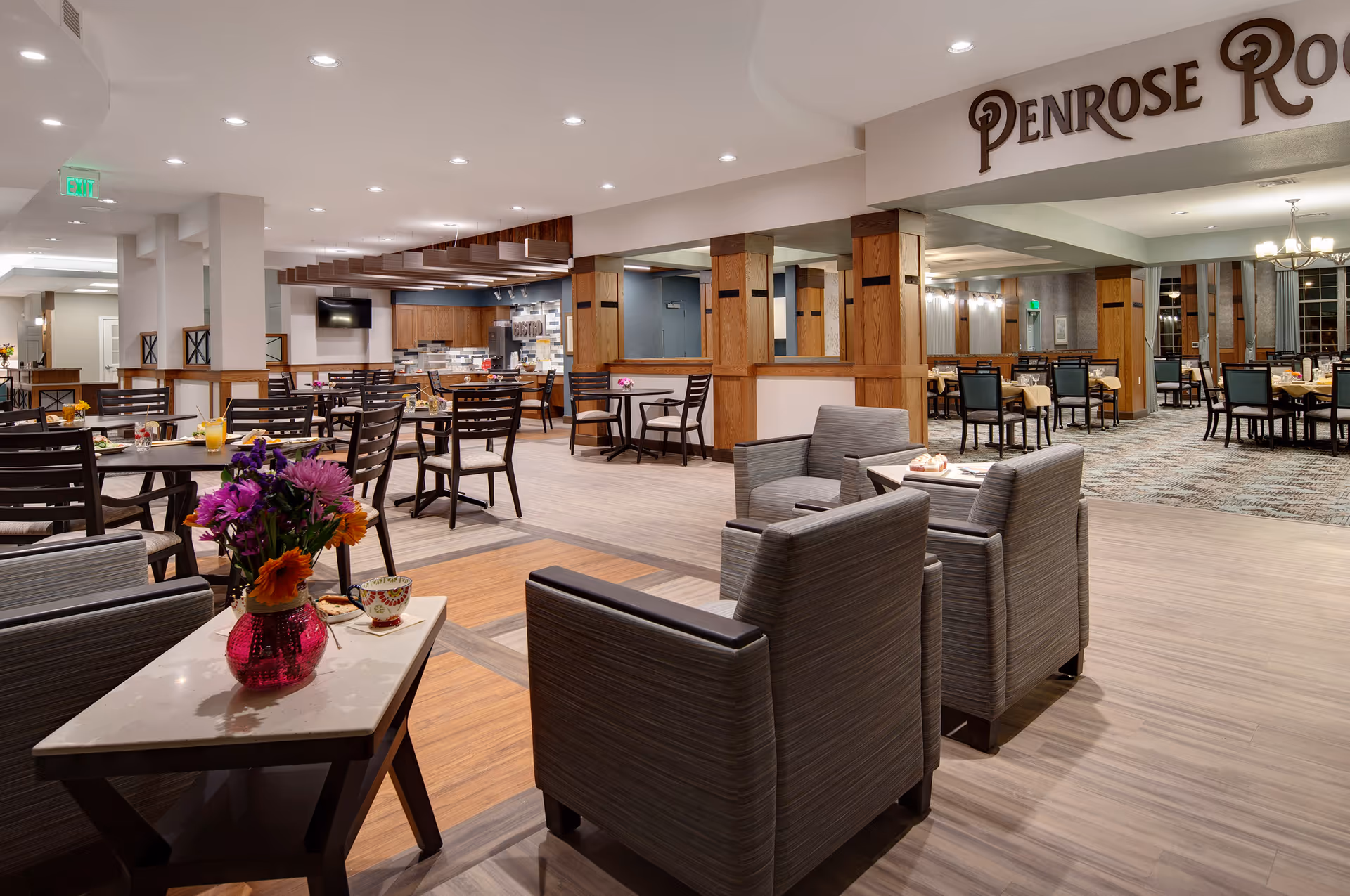 Open dining and lounge area with multiple tables and chairs, armchairs in the foreground, and a sign reading 'Penrose Room'.