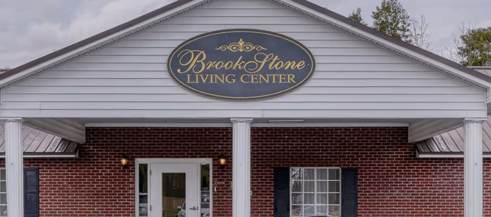 Entrance of Brook Stone Living Center showing a gabled portico with an oval name sign over a brick facade.