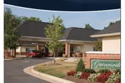 Exterior view of a single-story building with a covered entrance and a driveway. There are trees and landscaped bushes around the entrance area. A sign in front reads 'Gainesville'.