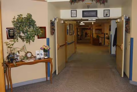 Interior hallway of a senior living facility with plants, a console table, and a welcoming sign.
