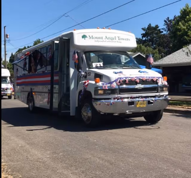 Decorated white bus with Mount Angel Towers sign driving on a sunny street