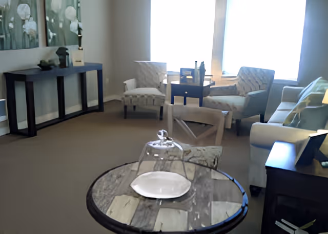 Well-lit seating area with armchairs, a sofa, side tables, and a round table with a glass cloche in the foreground.