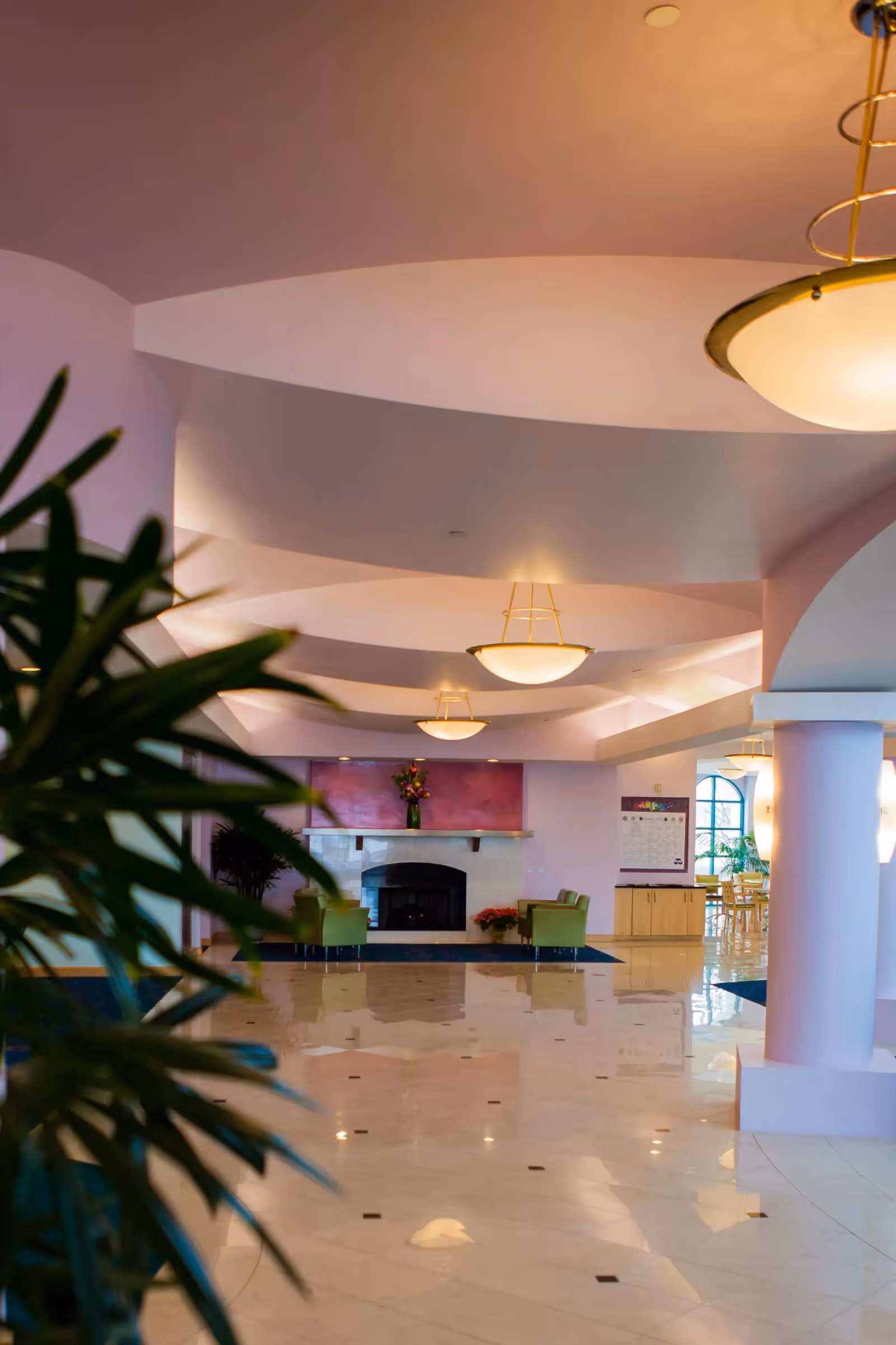 Bright curved-ceiling lobby with hanging lights, a fireplace, seating areas, and plants.