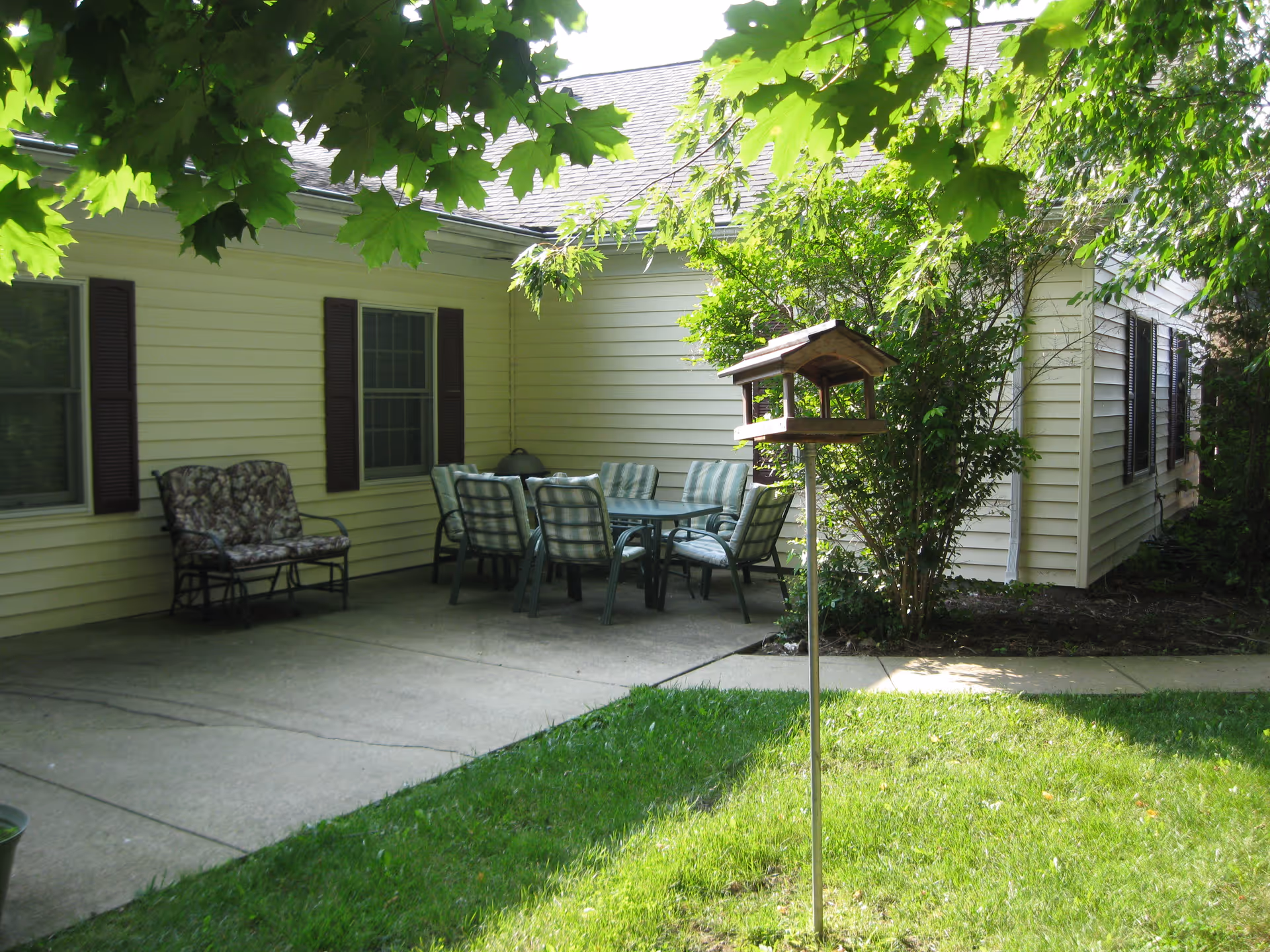 Patio area with outdoor table and chairs beside a beige house and green trees