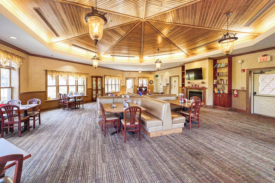 Bright communal dining room with booth seating, multiple tables, wood-paneled domed ceiling and pendant lights.